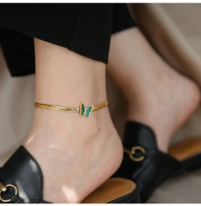 Close-up of golden anklet featuring a green enamel butterfly charm on model's ankle