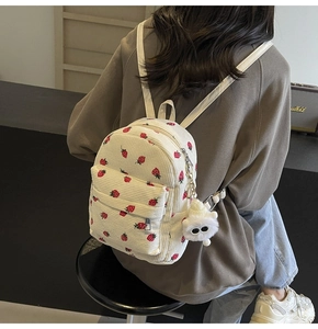Detail of white corduroy backpack with strawberry patterns and a side charm on model