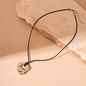 Detailed shot of irregular silver heart pendant on black cord over natural stone surface