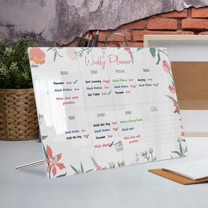 Detailed view of clear acrylic weekly planner board with floral designs on a desk