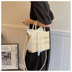 Beige straw handbag featuring a large white lace bow and woven handle detail