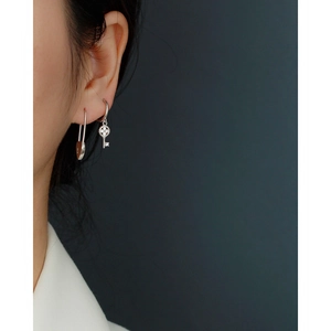Detail of S925 silver safety pin earring and clover key drop earring on a model