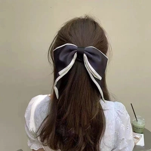 Detail view of a large black satin bow hair tie with white contrast piping on brown hair