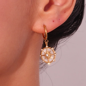 Détail de boucles d'oreilles boussole dorées avec nacre blanche et zircons