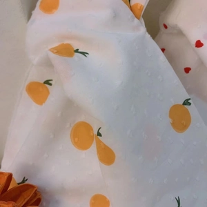 Detail of white fabric featuring orange fruit prints and 3D textured polka dot patterns