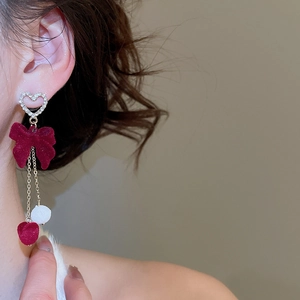 Detail view of long tassel earrings with red velvet bow and white pompon on model
