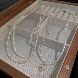 Detail view of pearl and silver bead necklaces with a heart pendant in a wooden jewelry box