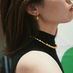 Close-up of model wearing minimalist golden teardrop earrings and beaded necklace