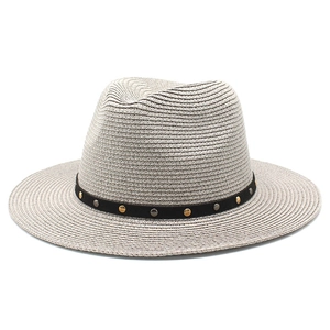 Detail of a beige woven Panama hat featuring a black band with gold and silver metal studs