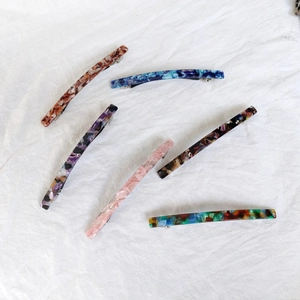 Detailed view of 10cm acetate hair clips with marble patterns on white fabric background