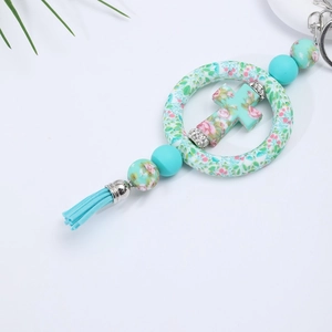 Detailed macro view of mint green silicone cross pendant with floral pattern and tassel