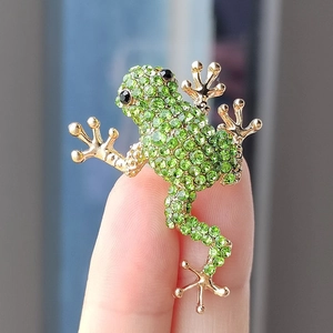 Close-up of green crystal frog brooch with gold plating held in hand for scale
