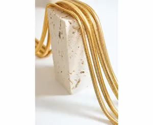Detailopname van een gouden platte slangenketting op een witte getextureerde steen