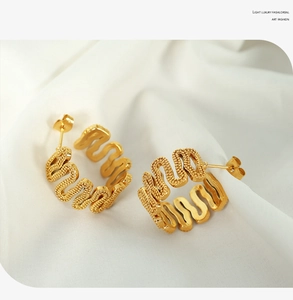 Macro detail of gold wavy C-shape earrings with beaded texture on white silk background