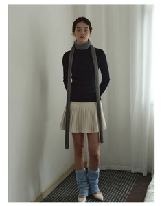 Detail of a thin grey knit long scarf paired with a blue sweater and white pleated skirt