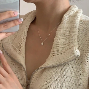 Close-up of a delicate gold shell pendant necklace with a pearl on a knit sweater