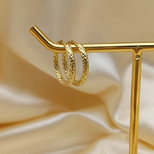 Detailed view of gold hoop earrings with hammered texture on a golden display stand