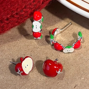 Asymmetric apple stud earrings with red enamel and green leaves on textured paper