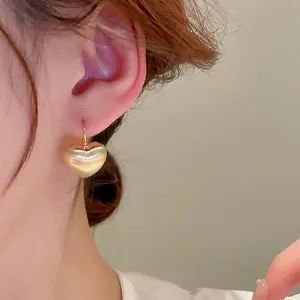 Gold-plated heart drop earrings with a matte brushed finish on a female model