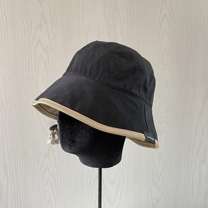 Detail of a black bucket hat with khaki trim, adjustable drawstring and brand label