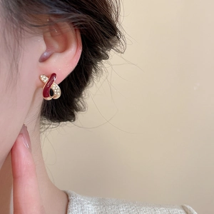 Detailed close-up of a red and gold crisscross earring with sparkling crystals on ear