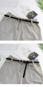 Close-up of a slim black leather belt with a metal buckle on light gray denim shorts