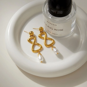 Détail de boucles d'oreilles infini dorées avec perles gouttes sur plateau blanc
