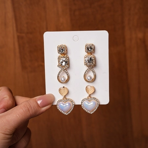 Detail of elegant gold earrings with rhinestones, pearls and iridescent heart shapes