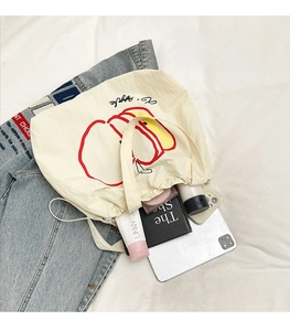 Macro detail of beige nylon tote bag with red apple print showing its large capacity