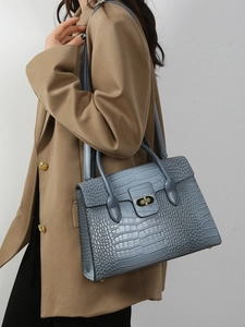Elegant crocodile-embossed haze blue handbag with gold twist-lock on stylish model