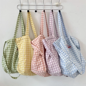 Five colorful gingham plaid tote bags hanging on a wall showing various color options