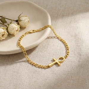 Elegant gold Ankh cross bracelet on beige linen cloth with decorative rose