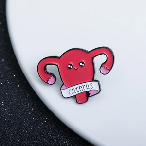 Cute red anatomical uterus enamel pin with cuterus ribbon on a dark glitter background