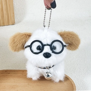 Mini plush puppy keychain with black glasses and a silver bell on a wooden tray