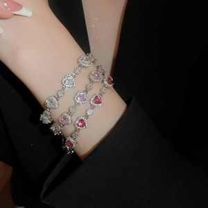 Detailed view of layered silver bracelets with pink heart-shaped zircon stones on a wrist