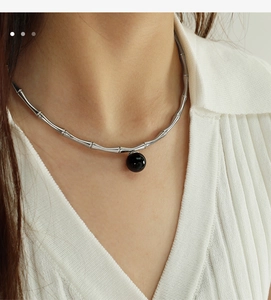 Close-up of a silver bamboo joint necklace with a minimalist black bead pendant on a model