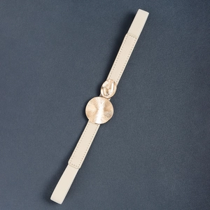Close-up of cream elastic skinny belt with textured gold double ring metal buckle
