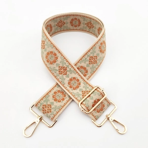 Embroidered floral bag strap with gold metal hardware on a minimalist white background