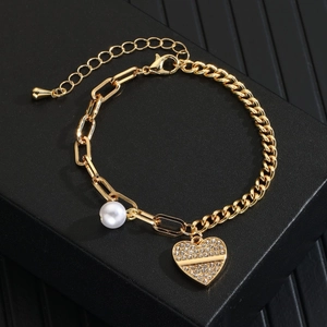 Detail of gold heart pendant with sparkling zircons and a white pearl on the bracelet