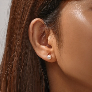 Detail of s925 silver pearl earring with red zircon stud worn on a female ear