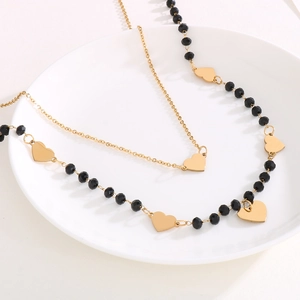 Close-up of double-layer gold necklace with black faceted beads and heart pendant on white plate
