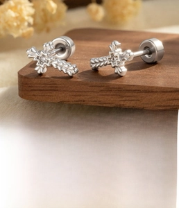 Detail view of gothic silver cross earring with zircon inlay on a dark wooden stand