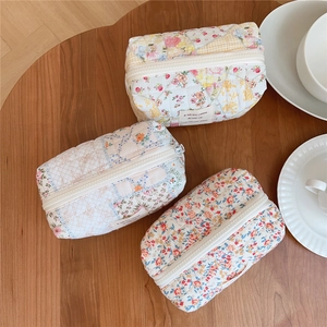 Detailed view of floral quilted cotton makeup bags in three colors on a wooden table