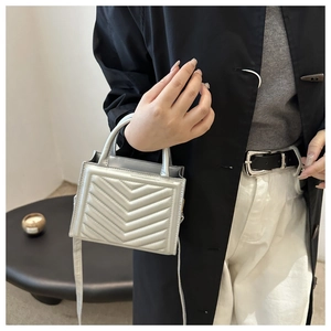 Detail of silver quilted mini crossbody bag with V-shaped texture on black coat background