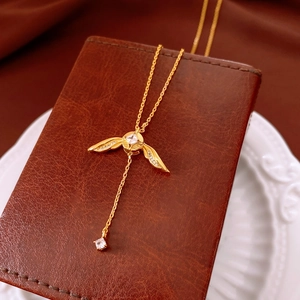 Détail macro du collier en Y doré avec pendentif ailé sur un coffret à bijoux