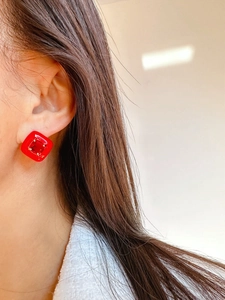Close-up of red square stud earring with textured enamel and faceted zircon on model
