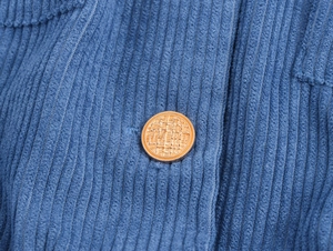 Macro shot of gold textured round button on vintage blue corduroy long dress