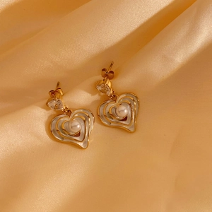 Elegant gold heart earrings with white enamel and center pearl on silk background