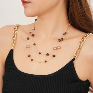 Detail view of layered gold chain necklace featuring tiger eye stones and lustrous pearls
