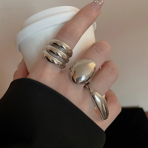 Detailed view of silver irregular liquid-style rings worn on hands holding a coffee cup